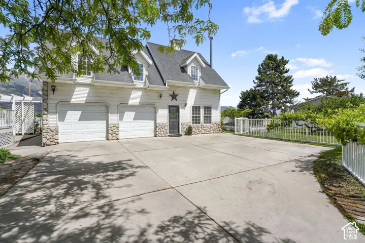 Two-story exterior featuring white horizontal siding, a stone veneer foundation, dormer windows, a dual-bay garage, and an expansive concrete driveway