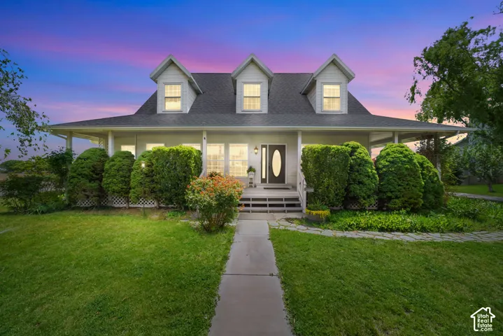 Two-story residence featuring a wrap-around porch, three roof dormers, a multi-pane front door with oval glass insert, and mature landscaping
