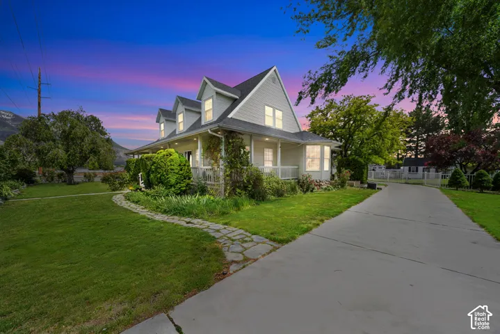 Two-story residence featuring light-colored horizontal siding, multiple roof dormers, a covered wrap-around porch, stone-path landscaping, and a concrete driveway