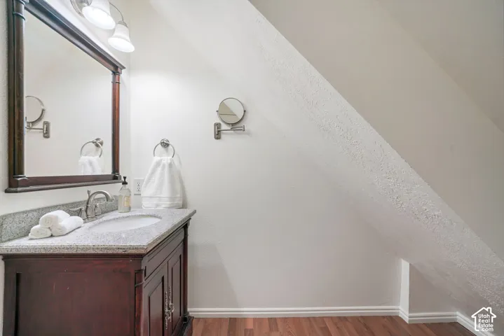 Wood-finish vanity featuring a stone countertop, oval undermount sink, matching framed mirror, multi-bulb overhead lighting, and an adjustable wall-mounted mirror