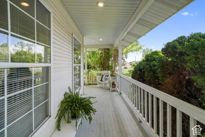 Covered porch featuring white vertical siding, recessed lighting, horizontal plank flooring, and a white picket-style railing