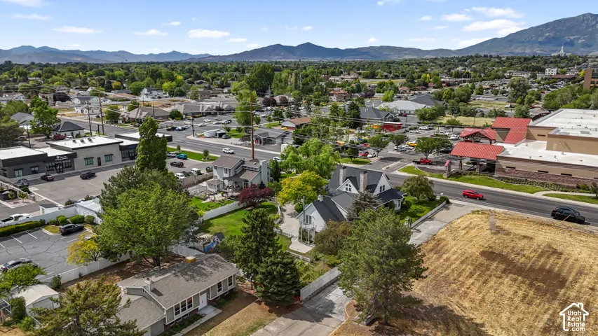 Aerial perspective featuring a multi-story residence with a pitched roofline, brick chimneys, and an expansive yard with mature landscaping, set against a prominent mountain backdrop