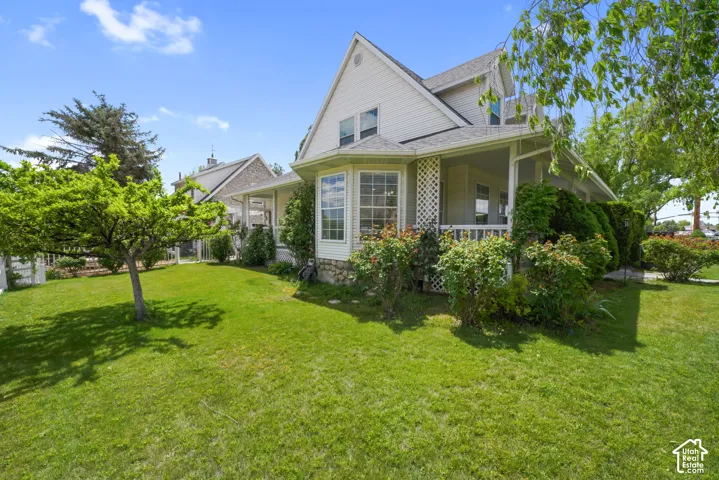 Two-story siding exterior featuring a wraparound covered porch, stone foundation detailing, and mature landscaping