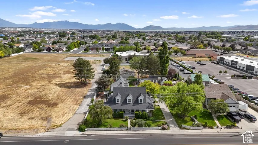 Aerial perspective featuring a multi-story residence with a pitched shingle roof, dormer windows, a covered front porch, and mature trees, set against a backdrop of mountain ranges