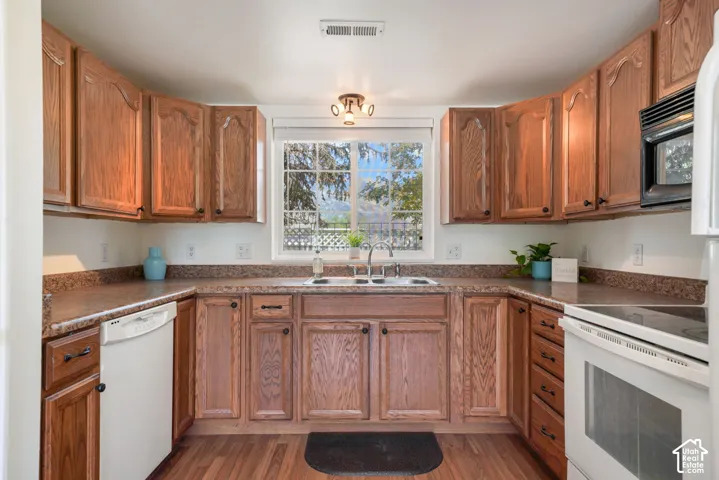 Kitchen featuring oak cabinetry, laminate countertops, a double-basin stainless steel sink, built-in dishwasher, and wood-finish flooring