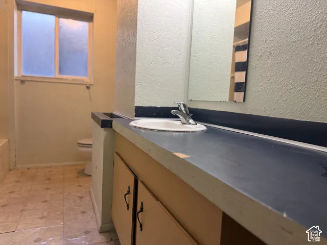 Bathroom featuring a vanity with a solid-surface countertop, an integrated sink, metal faucet hardware, a wall-mounted mirror, and tile flooring