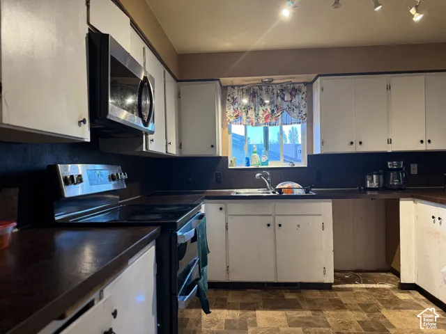 Kitchen featuring white cabinetry, dark solid-surface countertops, built-in stainless steel microwave, stainless steel range, and track lighting
