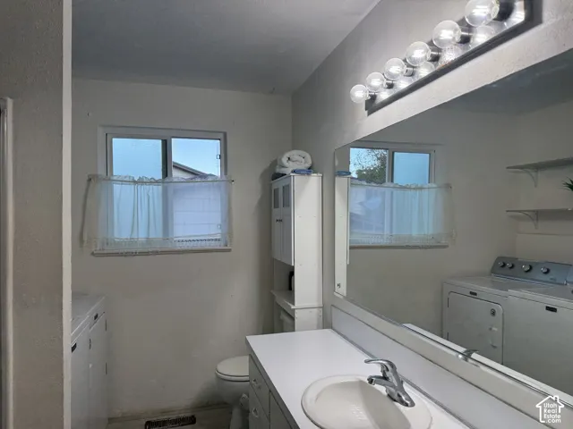 Bathroom featuring a vanity with integrated sink, expansive wall-mounted mirror, overhead multi-bulb lighting, and built-in shelving