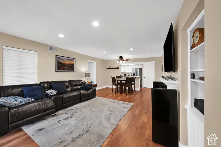 Open living area featuring wood-finish flooring, recessed lighting, a white built-in bookshelf, and a fireplace mantel