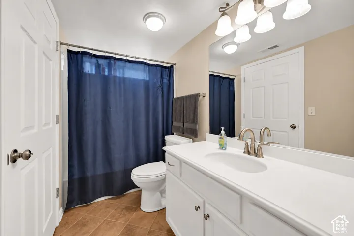 Bathroom featuring a white vanity with an integrated sink, polished metal faucet, large wall-mounted mirror, multi-bulb overhead lighting, and tile flooring