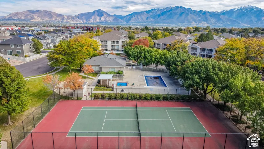 Fenced tennis court, outdoor swimming pool, and spa area set against a mountain backdrop with mature trees and landscaped grounds