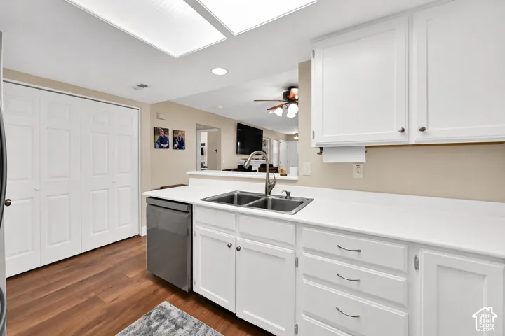 Kitchen featuring white cabinetry, wood-finish flooring, double-basin stainless steel sink with high-arch faucet, and white countertops