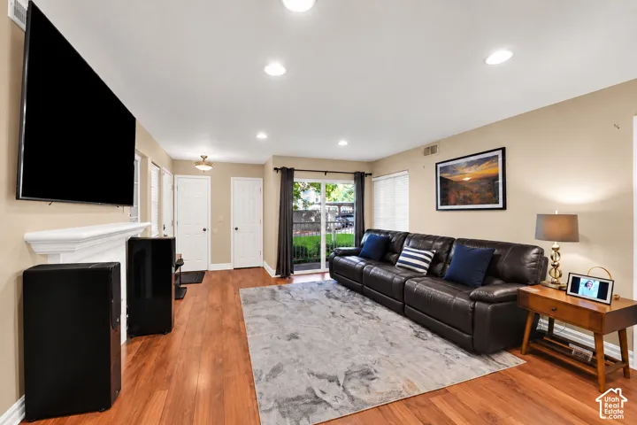 Living area featuring wood-finish flooring, recessed lighting, a fireplace with a white mantel, and glass sliding doors
