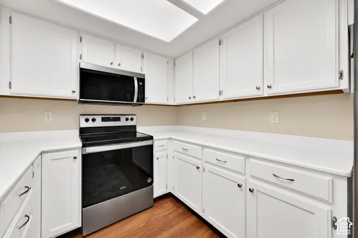 Kitchen featuring white cabinetry, solid surface countertops, stainless steel electric range, stainless steel microwave, and wood-finish flooring