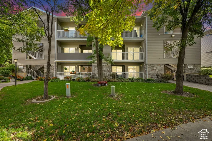 Multi-story residential building exterior featuring horizontal siding, stone veneer base, private balconies with metal railings, and concrete staircases