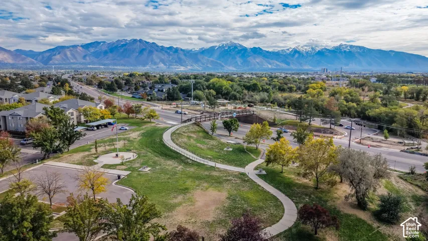 Aerial perspective featuring a paved walking path, mature trees, open green space, and a mountainous backdrop