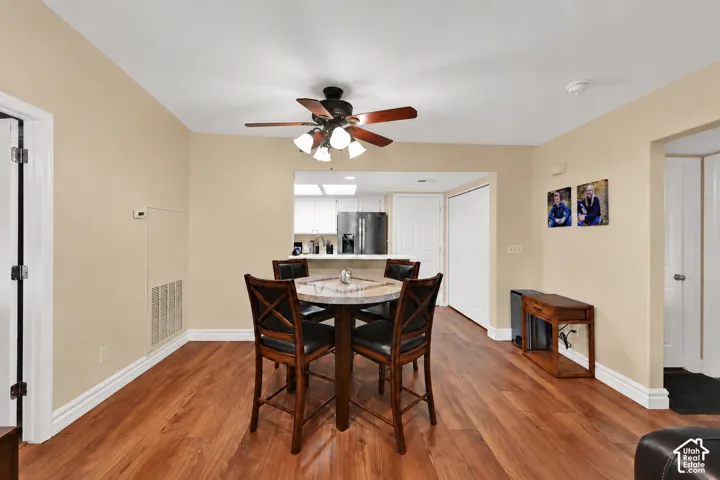 Wood-finish flooring, ceiling fan with integrated lighting, and pass-through opening to the kitchen