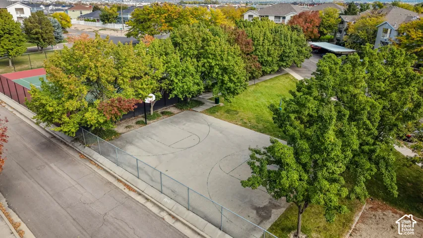 Outdoor recreation area featuring a concrete basketball court, a fenced tennis court, and mature landscaping