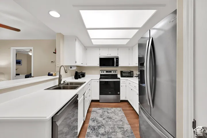 Kitchen featuring white shaker-style cabinetry, solid-surface countertops, stainless steel appliances, recessed lighting, and wood-finish flooring
