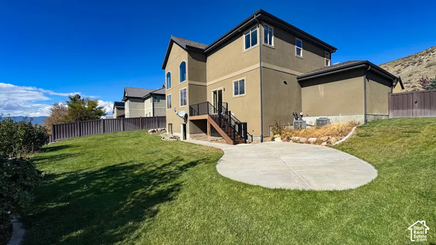Stucco exterior with multi-level rooflines, elevated wood deck with metal railing, concrete patio, and fenced yard