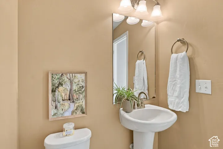 Pedestal sink with a polished metal faucet, wall-mounted vanity mirror, and three-bulb vanity lighting fixture