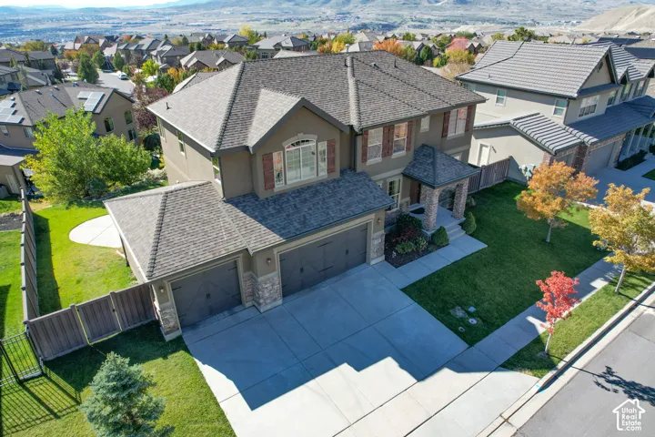 Two-story residence featuring a multi-gable roofline, stone veneer accents, three-car garage, and fenced backyard with mature landscaping