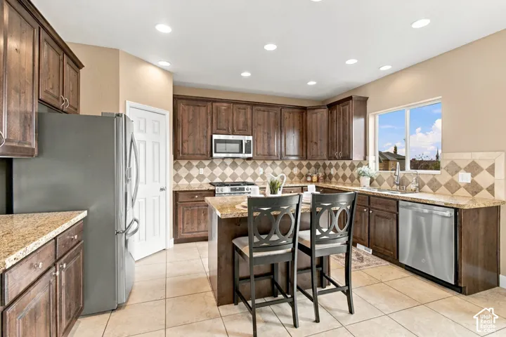 Kitchen featuring dark wood cabinetry, stone-finish countertops, stainless steel appliances, a center island, and a tile backsplash with a diamond pattern