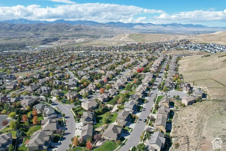 Aerial perspective of a residential neighborhood featuring paved streets, mature trees, manicured lawns, and a mountainous backdrop
