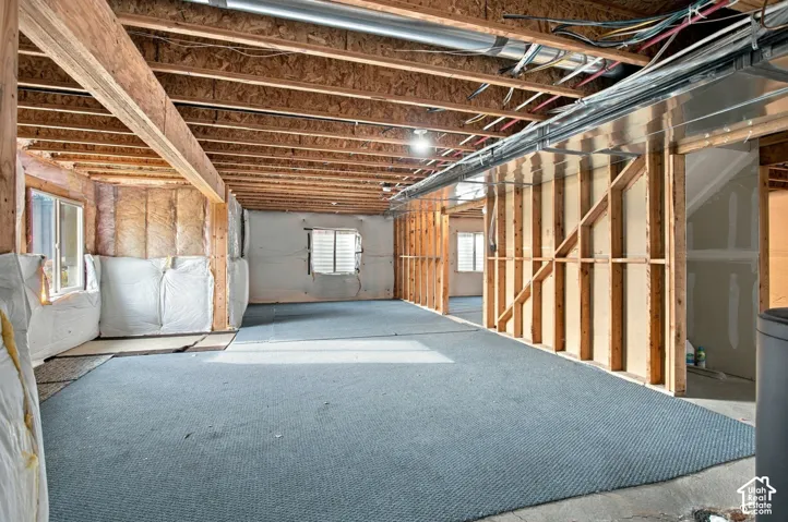 Unfinished lower level featuring exposed wood joist ceilings, wall-mounted fiberglass insulation, exposed wood stud framing, and three windows