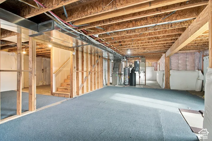 Unfinished lower level featuring exposed wood joists, partial stud framing, a staircase with wooden railings, and integrated mechanical systems