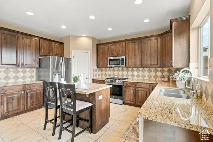 Kitchen featuring stained wood cabinetry, stone-finish countertops, a central island, diamond-pattern tile backsplash, and stainless steel appliances