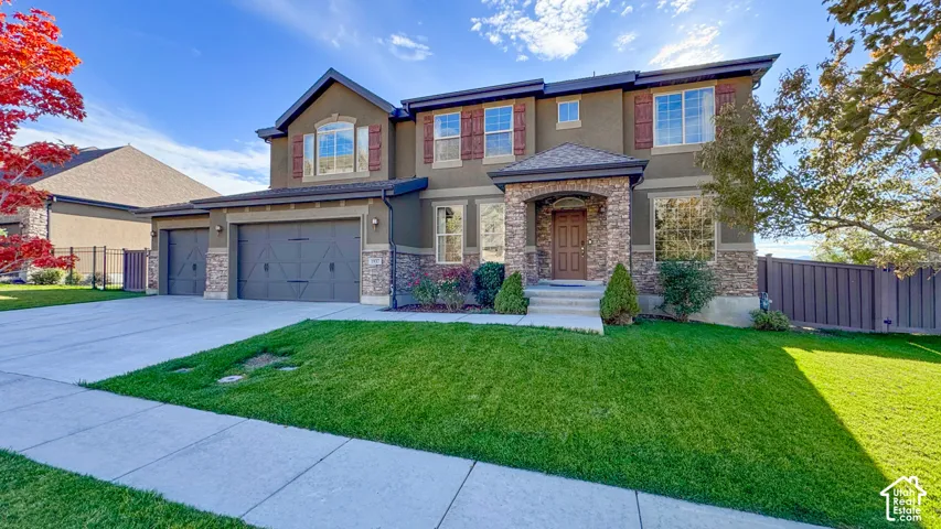 Two-story exterior featuring a stone veneer facade, shingle roof, decorative shutters, a three-car garage, and a covered front entry