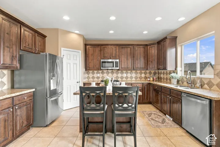 Kitchen featuring stained wood cabinetry, stone countertops, diamond-patterned tile backsplash, stainless steel appliances, and tile flooring