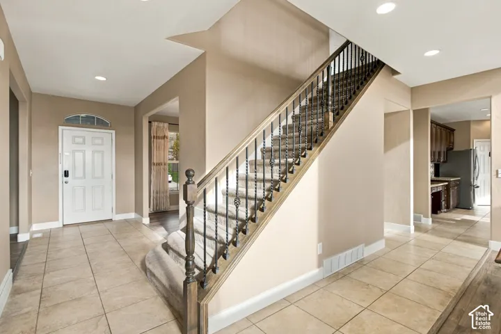 Foyer featuring tile flooring, staircase with metal balusters, wooden handrail, and recessed lighting