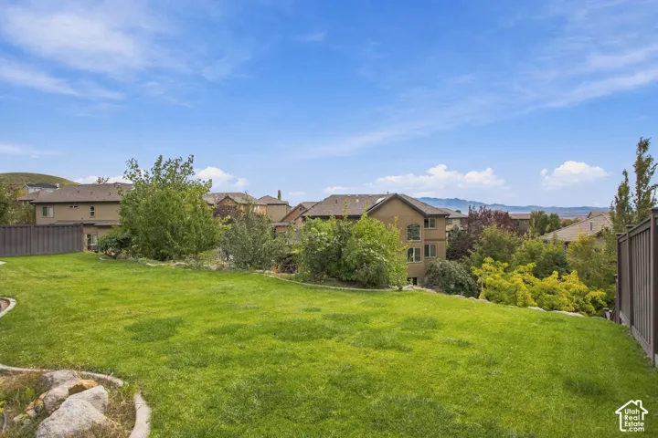 Expansive backyard featuring a manicured lawn, stone hardscaping, mature trees, and perimeter privacy fencing