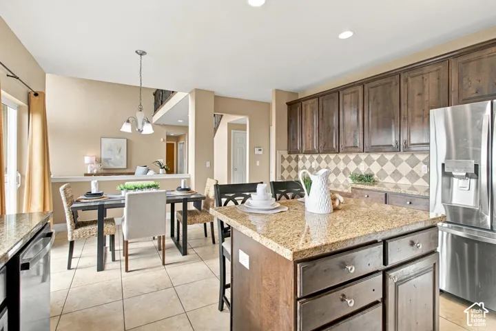Kitchen featuring stained wood cabinetry, stone countertops, central island, diamond-patterned tile backsplash, and stainless steel refrigerator