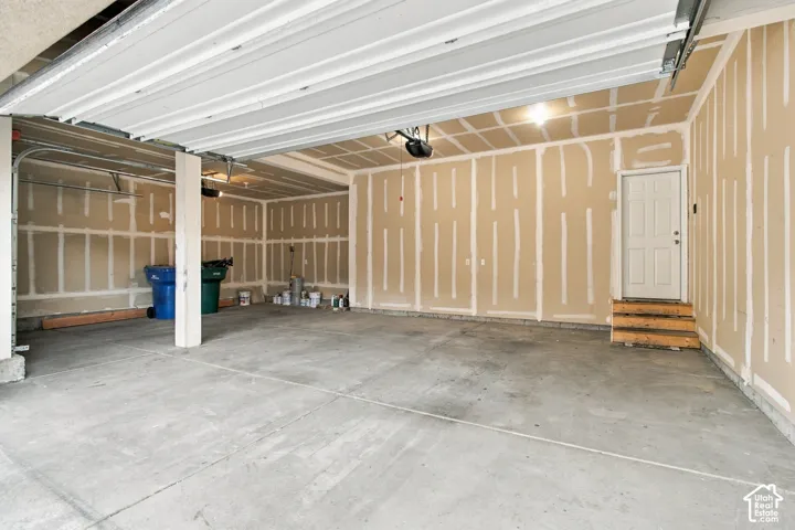 Attached multi-car garage featuring a concrete floor, high-clearance overhead door, unfinished drywall, and a dedicated pedestrian access door with wood-framed stairs