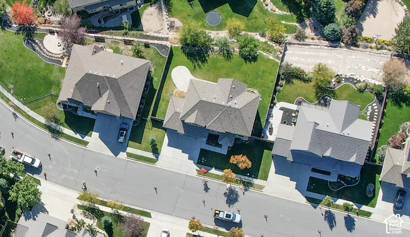 Aerial perspective of a residential property featuring a concrete driveway, multi-gabled roofline, manicured lawn, and hardscaped rear patio area