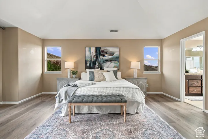 Neutral-toned interior featuring wood-finish flooring, a vaulted ceiling, dual windows with mountain scenery, and an open doorway to a bathroom with dark-toned cabinetry