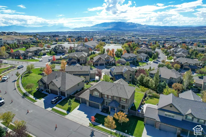 Aerial perspective of a multi-level suburban residence featuring a multi-car garage, asphalt-shingled roof, manicured lawn, and proximity to expansive mountain and valley scenery