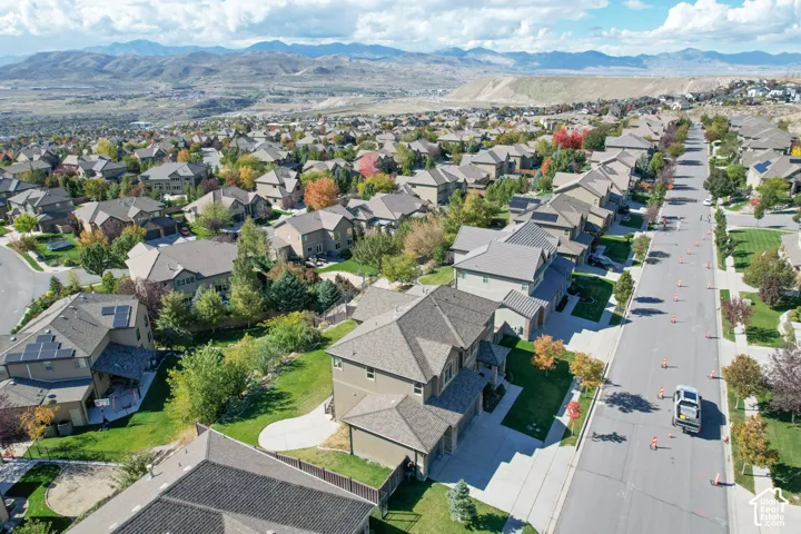 Aerial perspective of the residential neighborhood featuring multi-level homes, asphalt streets, manicured lawns, and a distant mountain range backdrop
