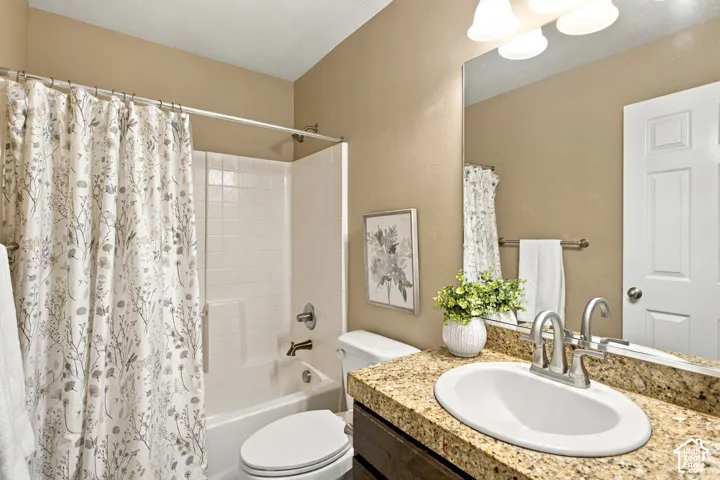 Bathroom featuring a vanity with stone-finish countertop, oval undermount sink, three-light fixture, mirror, and a tub-shower combination with tile-finish surround