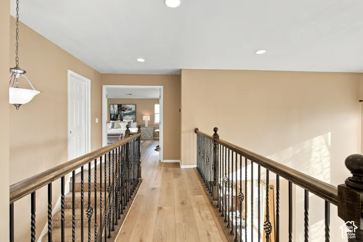 Hallway featuring wood-finish flooring, metal spindle balusters with stained wood railings, recessed lighting, and a pendant fixture