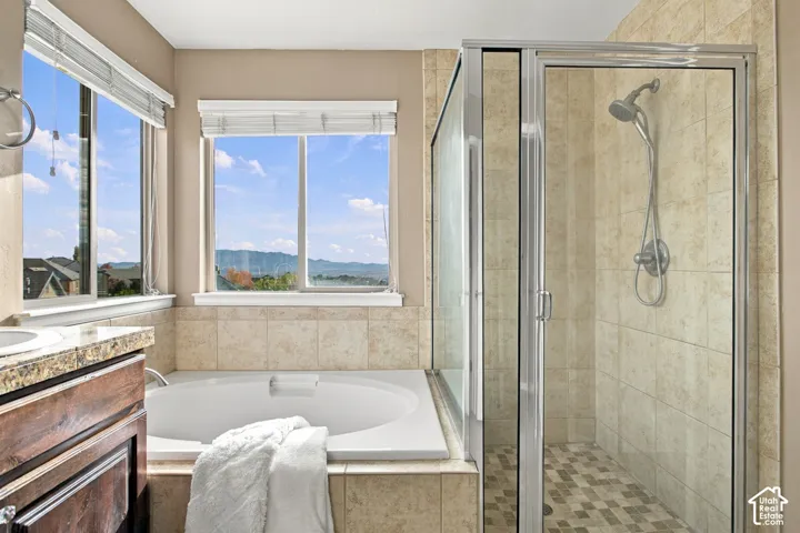 Bathroom featuring a deep soaking tub, separate glass-enclosed shower, stone-tile surround, mountain backdrop, and dual-pane windows