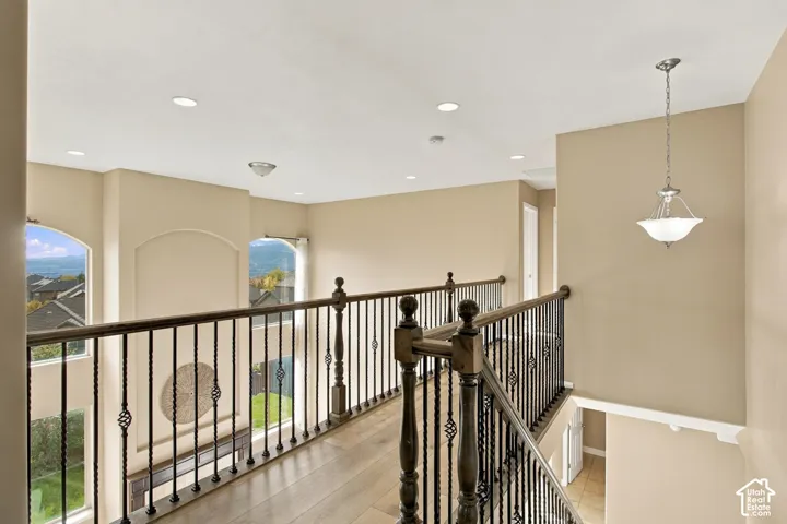 Elevated walkway featuring wood-finish flooring, metal balusters with decorative iron scrolls, arched windows, and recessed lighting