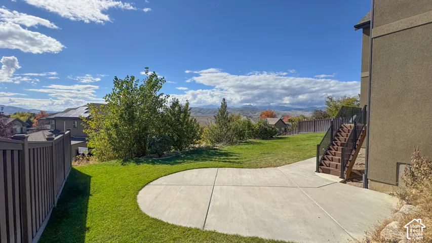 Backyard featuring a concrete patio, grassy lawn, wood-stain staircase, and privacy fencing, set against a mountain backdrop
