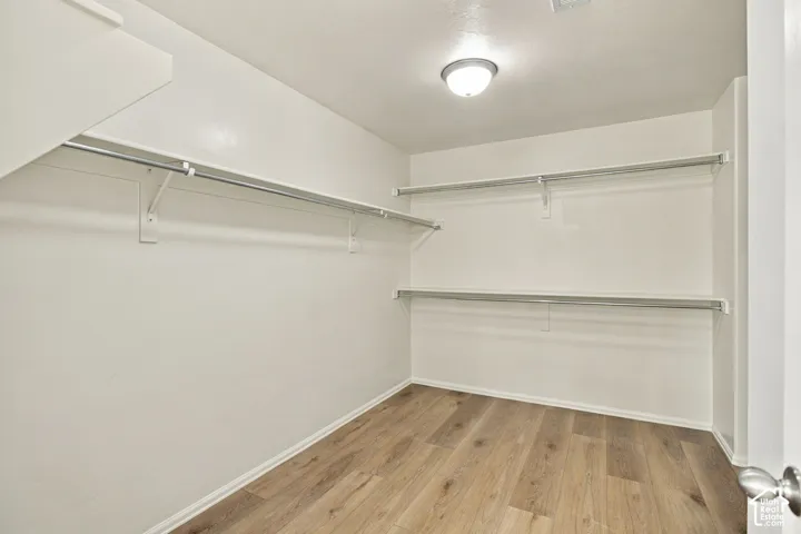 Storage area featuring wood-finish flooring, dual-tier shelving with hanging rods, and a ceiling-mounted flush light fixture