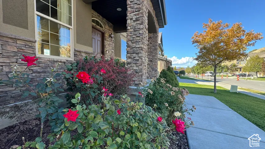 Exterior facade featuring stacked stone masonry, a covered porch entrance, divided-light windows, and landscaped garden beds with flowering shrubs