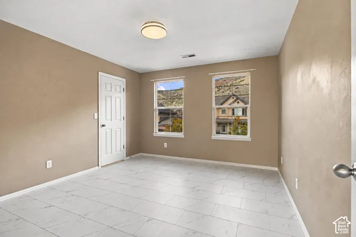 Neutral-toned interior space featuring light-colored stone-finish flooring, two large windows, and a multi-panel interior door