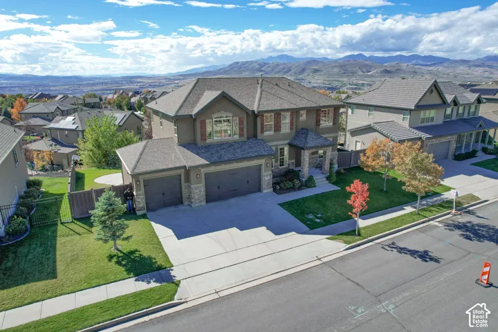 Multi-level exterior featuring a multi-car garage, stone masonry accents, a shingled roof, and a landscaped lot with mountain scenery